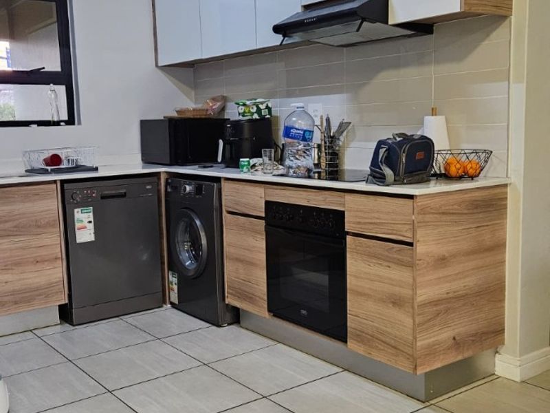 A modern kitchen featuring wood-grain and white cabinetry, stone countertops, built-in oven, extractor fan, and tiled flooring.