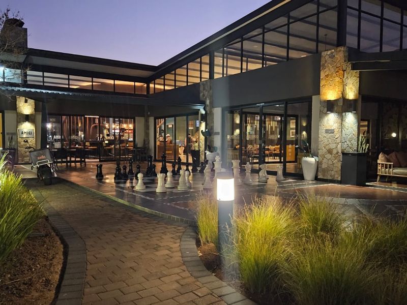 Modern clubhouse exterior featuring stone cladding, expansive glass sliding doors, and a paved walkway, illuminated by ambient outdoor lighting at dusk.