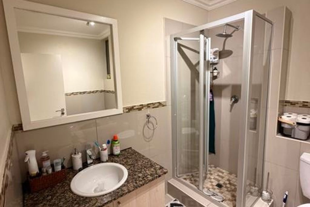 A well-maintained bathroom featuring a granite-topped vanity, a glass-enclosed shower, and neutral tile finishes throughout.