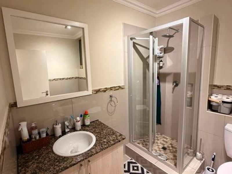 A well-maintained bathroom featuring a granite-topped vanity, a glass-enclosed shower, and neutral tile finishes throughout.