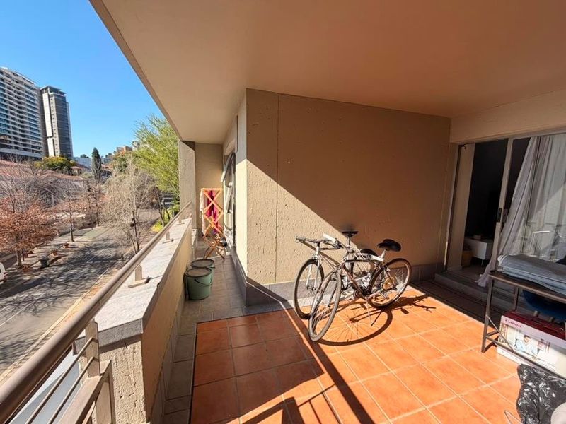 A spacious covered balcony featuring tiled flooring and a metal balustrade, offering an elevated view of the surrounding urban area.