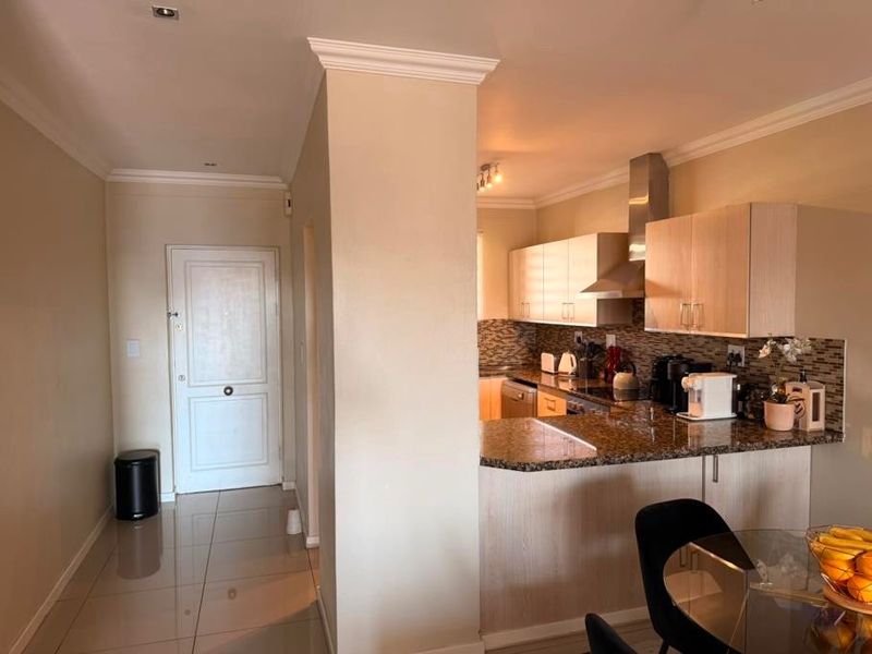 Open plan kitchen featuring granite countertops, mosaic backsplash, and modern cabinetry, seamlessly flowing into the entrance hallway with tiled flooring throughout.