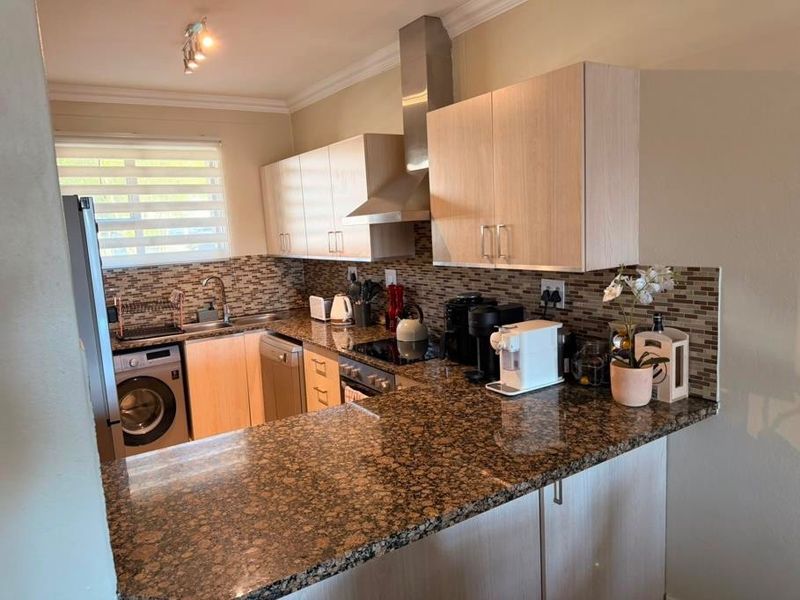 Functional kitchen featuring granite countertops, mosaic tile backsplash, built-in cabinetry, stainless steel extractor fan, and integrated appliances including a washing machine and oven.