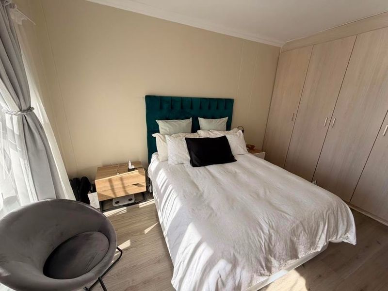 A well-maintained bedroom featuring light-toned laminate flooring and extensive built-in cupboards, providing ample storage space within a neutral, bright setting.