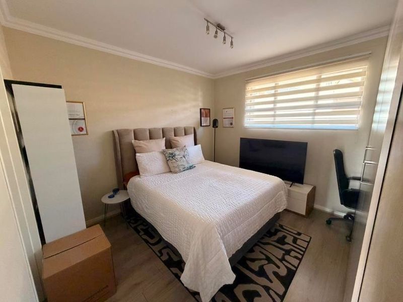 A well-maintained bedroom featuring laminate flooring, neutral wall tones, built-in wardrobe storage, and adjustable roller blinds for natural light control.