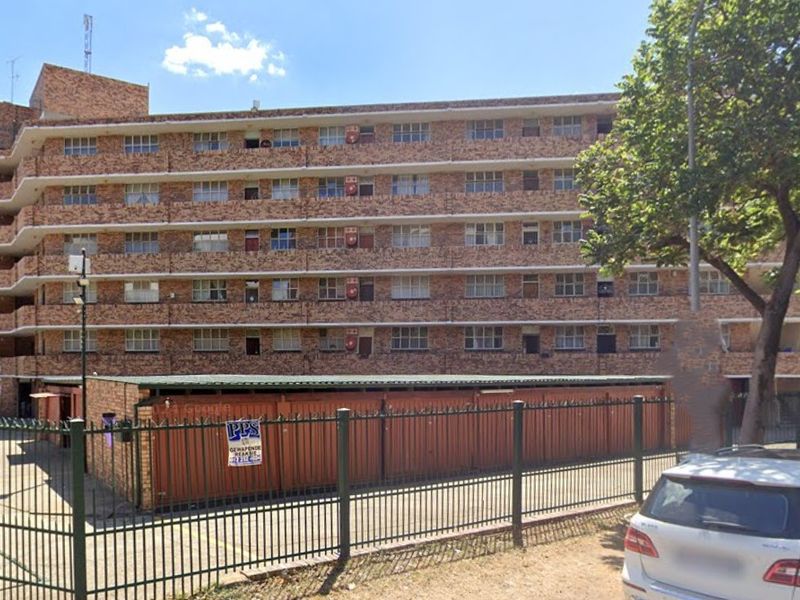 Street view of a multi-story brick apartment building featuring secure perimeter fencing and ground-level garage units.