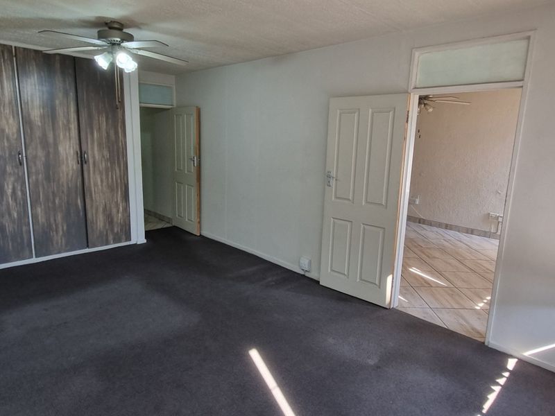 An empty bedroom featuring built-in cupboards, a ceiling fan, and carpeted flooring, offering a blank canvas for potential updates.