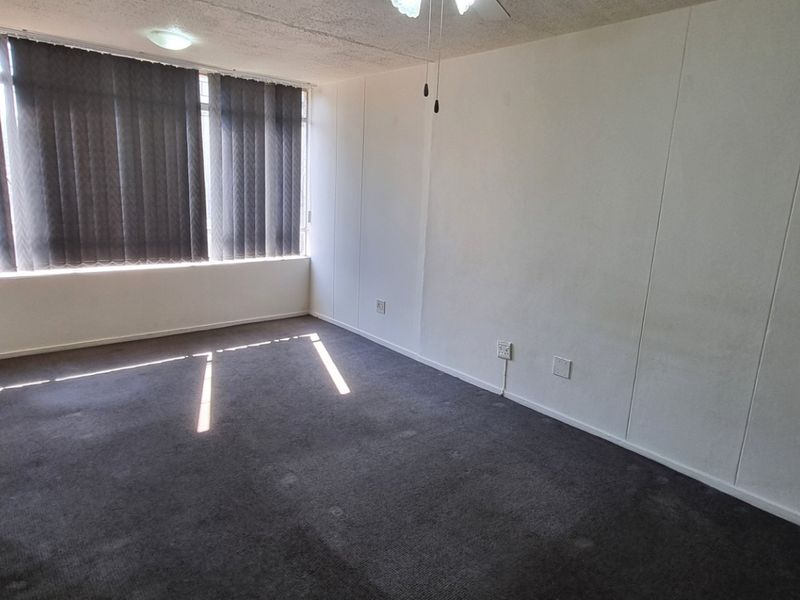 An empty bedroom featuring carpeted flooring, a ceiling fan, and large windows with vertical blinds, offering a blank canvas for potential updates.
