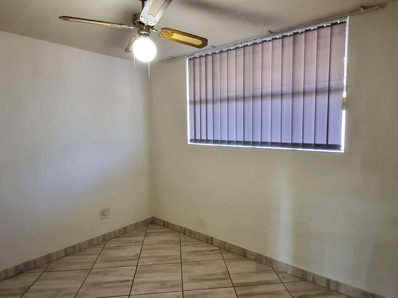 An empty bedroom featuring tiled flooring, a ceiling fan, and vertical window blinds, providing a clean and neutral space ready for personalization.