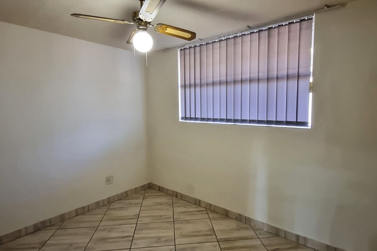 An empty bedroom featuring tiled flooring, a ceiling fan, and vertical window blinds, providing a clean and neutral space ready for personalization.