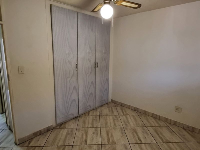 A vacant bedroom featuring built-in cupboards, a ceiling fan, and tiled flooring, offering a clean and functional space ready for personalization.