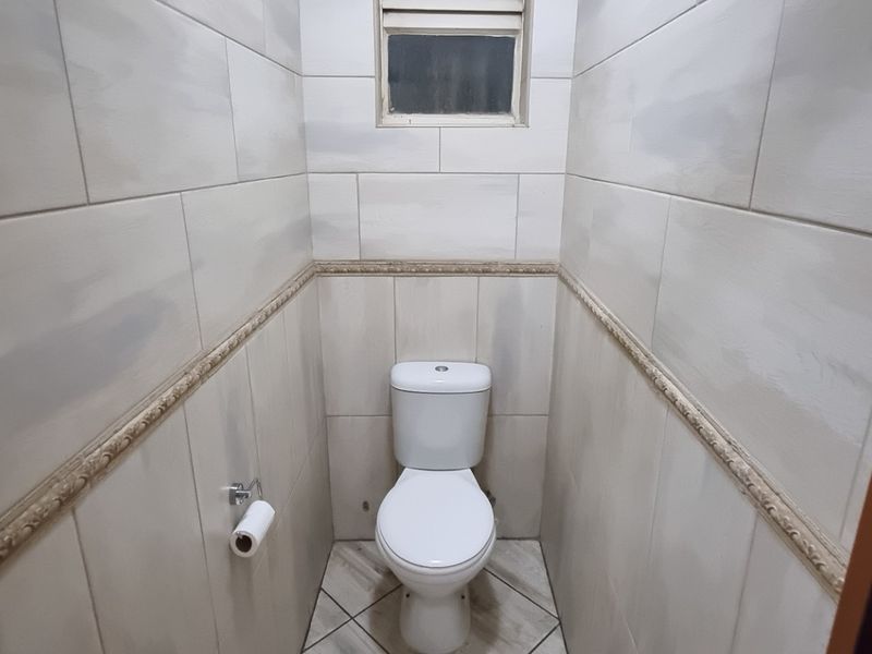 A compact, tiled guest bathroom featuring a modern toilet and a small high-level window for ventilation.
