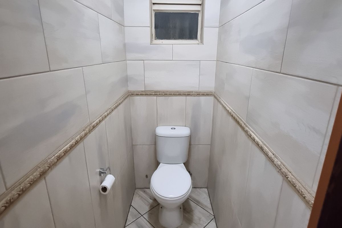 A compact, tiled guest bathroom featuring a modern toilet and a small high-level window for ventilation.