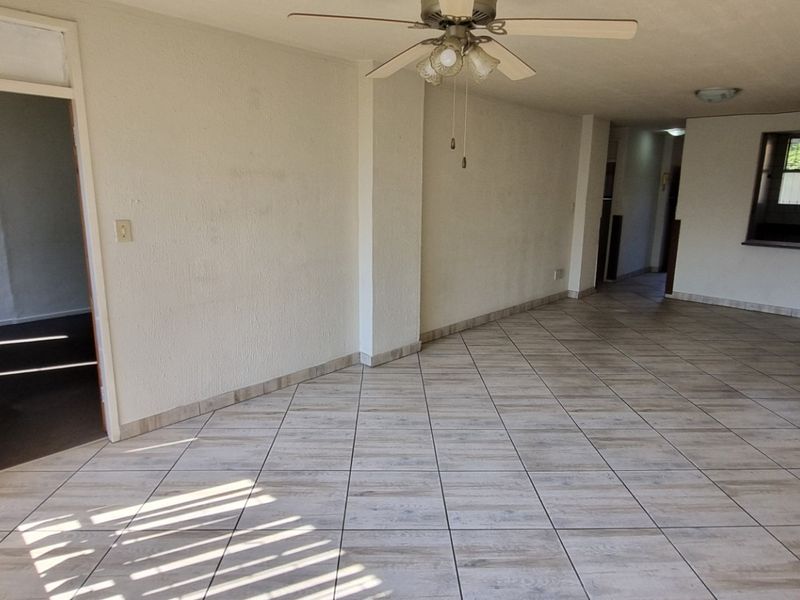 An empty open-plan living area featuring tiled flooring, a ceiling fan, and a convenient pass-through window connecting to the kitchen space.