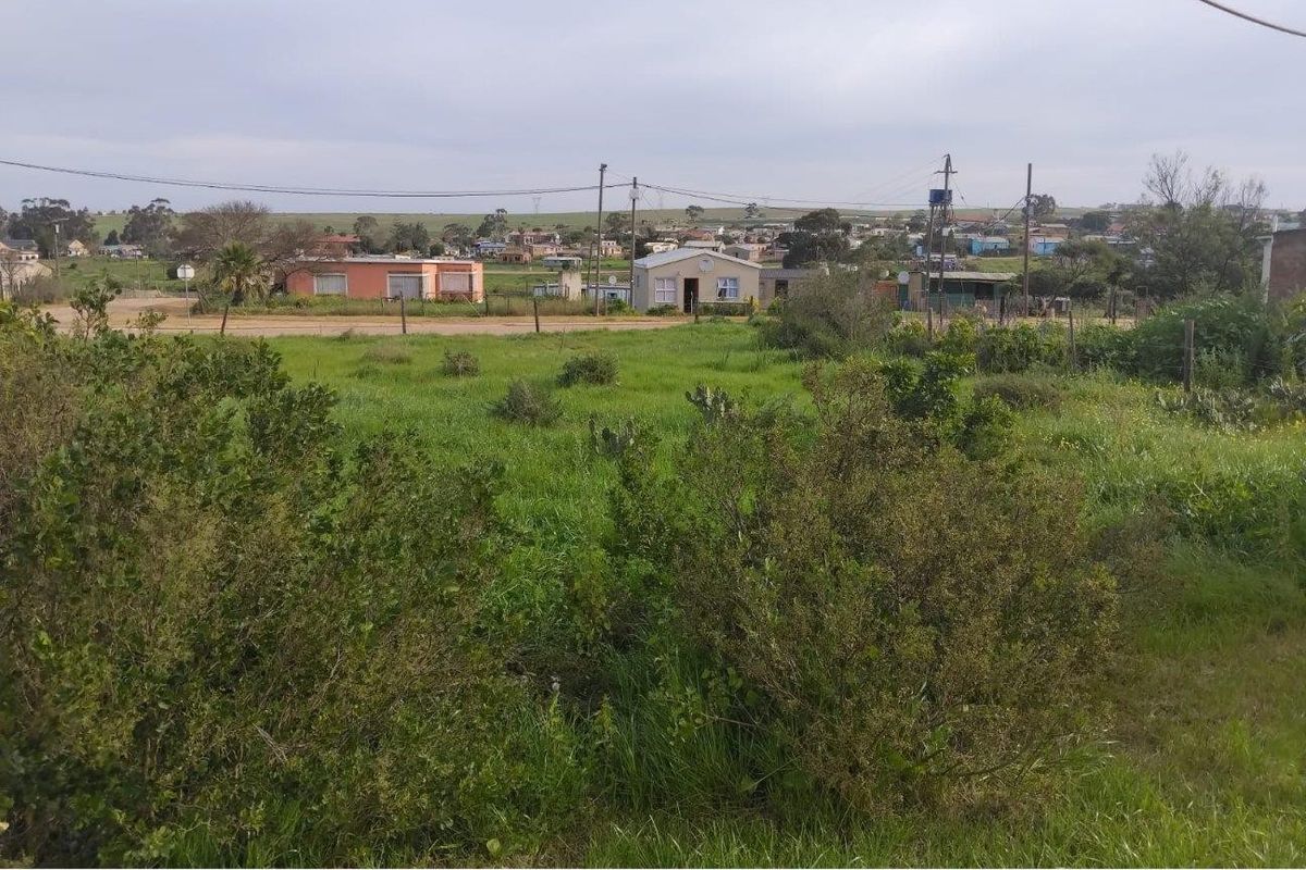 A view of a vacant residential plot featuring natural vegetation and perimeter fencing, situated in a developed neighborhood setting.