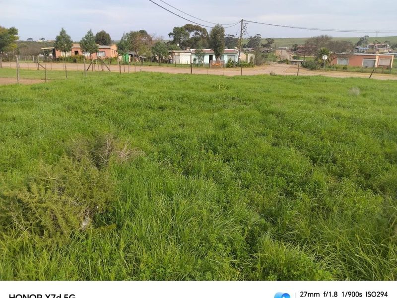 A vacant residential plot of land featuring grass cover, perimeter wire fencing, and access to nearby street infrastructure.