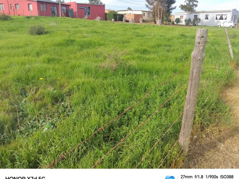 A vacant residential plot featuring grassy terrain enclosed by a rustic barbed wire fence with wooden posts.