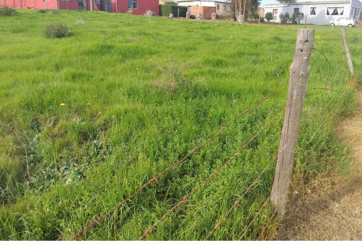 A vacant residential plot featuring grassy terrain enclosed by a rustic barbed wire fence with wooden posts.