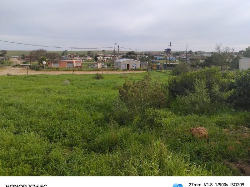 A view of an undeveloped residential plot featuring natural grassland with surrounding neighbourhood infrastructure visible in the distance.