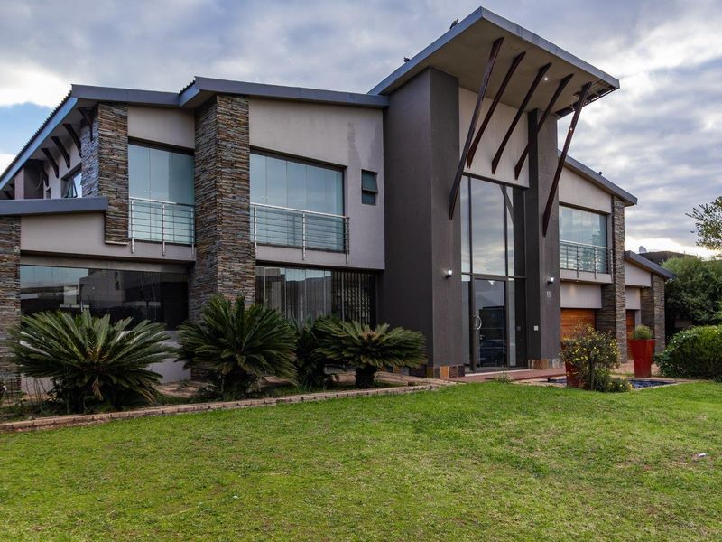 Modern double-storey residence featuring striking stone cladding, expansive glass windows, a prominent entrance, and a well-maintained front garden.