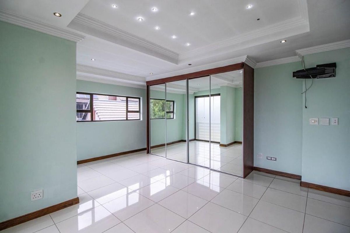 Spacious bedroom featuring large built-in mirrored wardrobes, recessed ceiling lighting, and polished tiled flooring throughout.