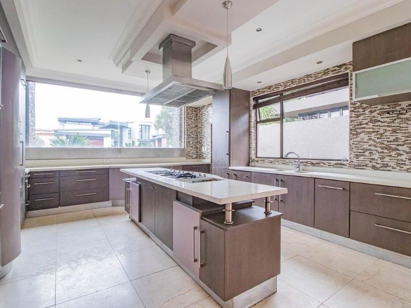Modern kitchen featuring a central island with gas hob, stone countertops, mosaic tile backsplash, and ample cabinetry with integrated appliances.