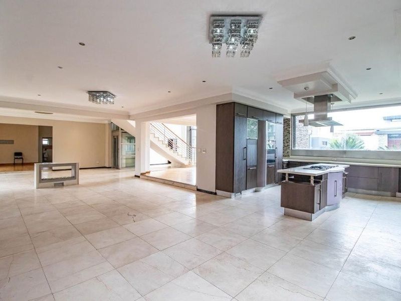 Spacious open-plan living area featuring large format floor tiles, a modern kitchen with a central island, and a feature staircase with glass balustrades.