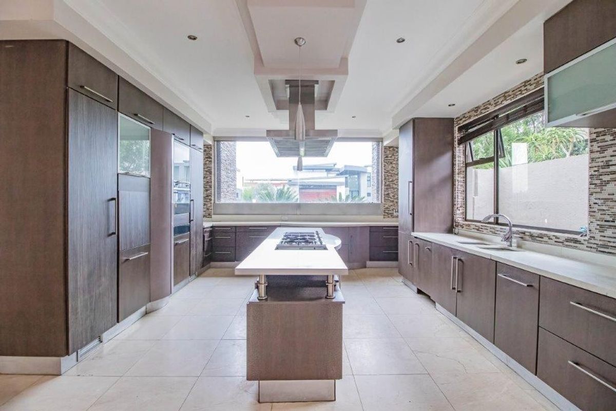 Modern kitchen featuring a central island with integrated cooktop, sleek cabinetry, mosaic backsplash, and high-end built-in appliances in a spacious, well-lit layout.