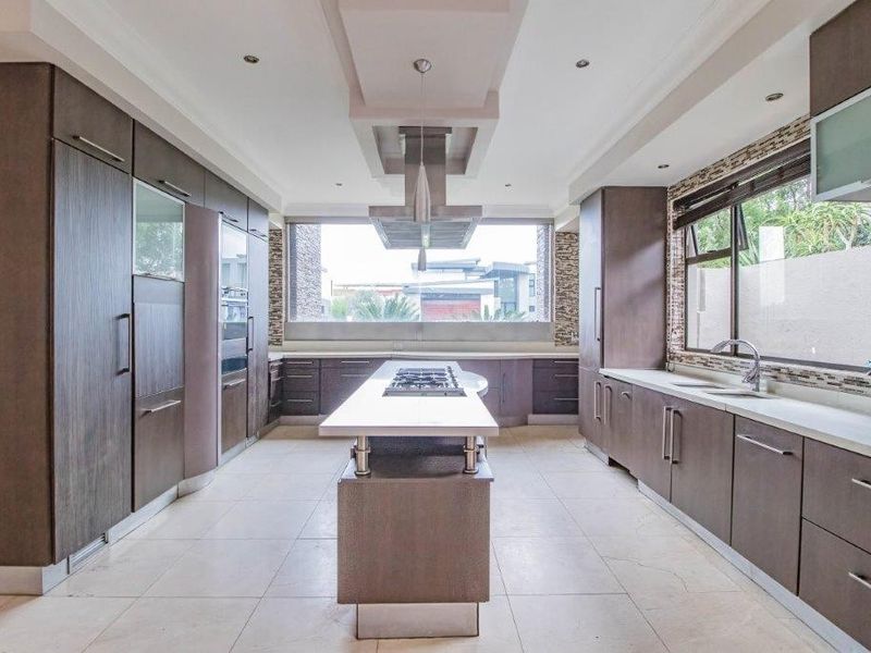 Modern kitchen featuring a central island with integrated cooktop, sleek cabinetry, mosaic backsplash, and high-end built-in appliances in a spacious, well-lit layout.