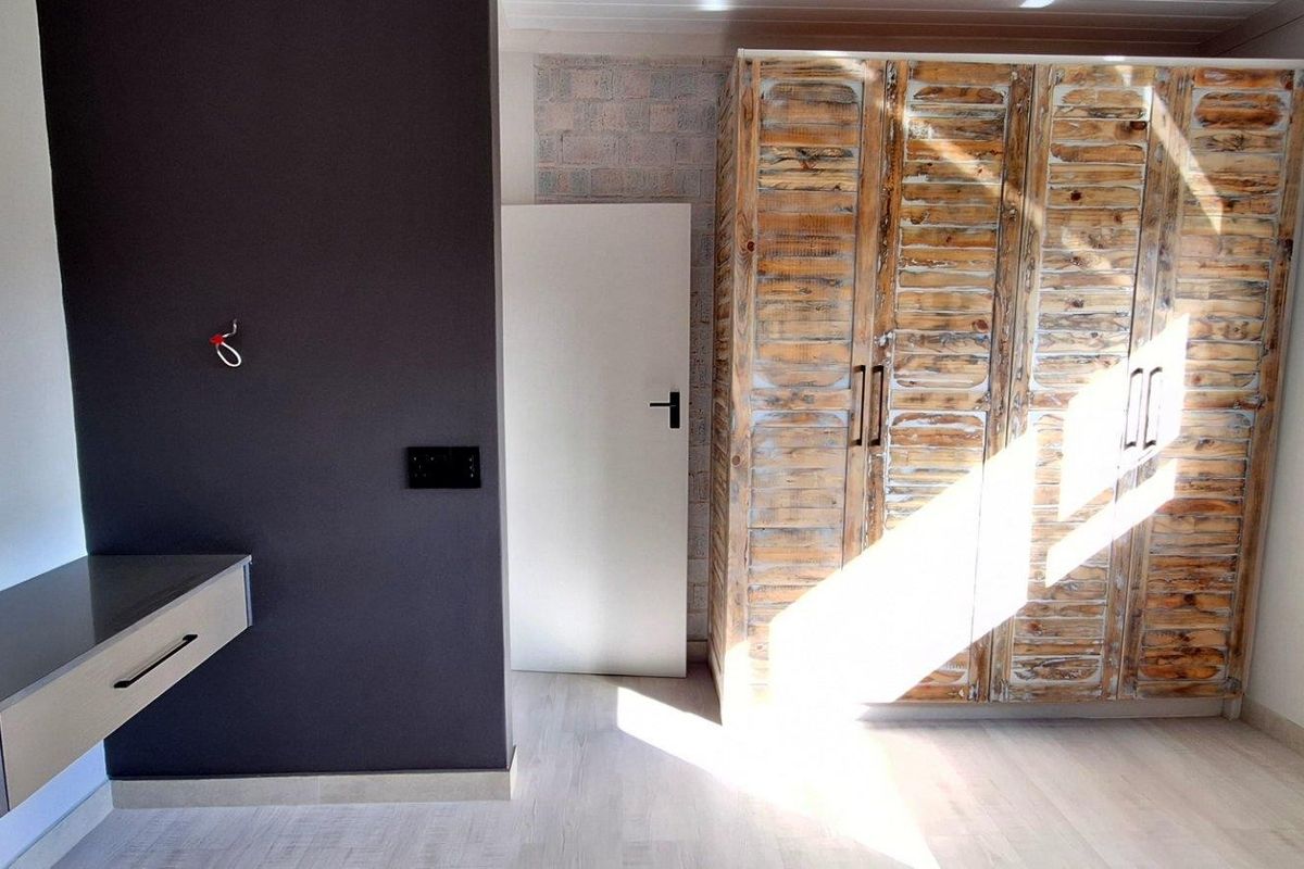 A bright bedroom featuring a built-in wooden wardrobe, a floating desk, and modern laminate flooring with natural light.