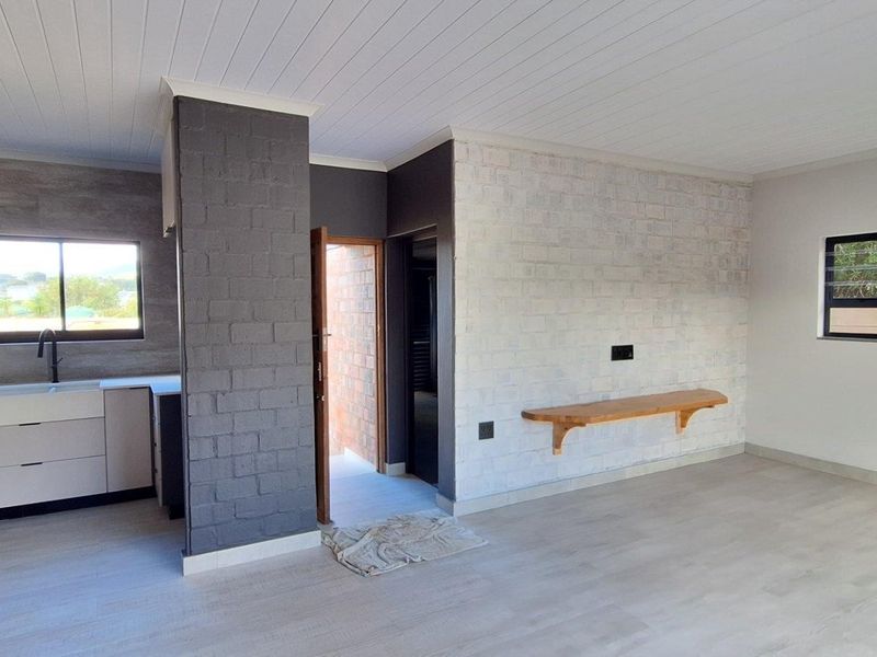 Modern open-plan living area featuring a sleek kitchen with built-in oven and hob, complemented by an exposed brick feature wall and light laminate flooring.