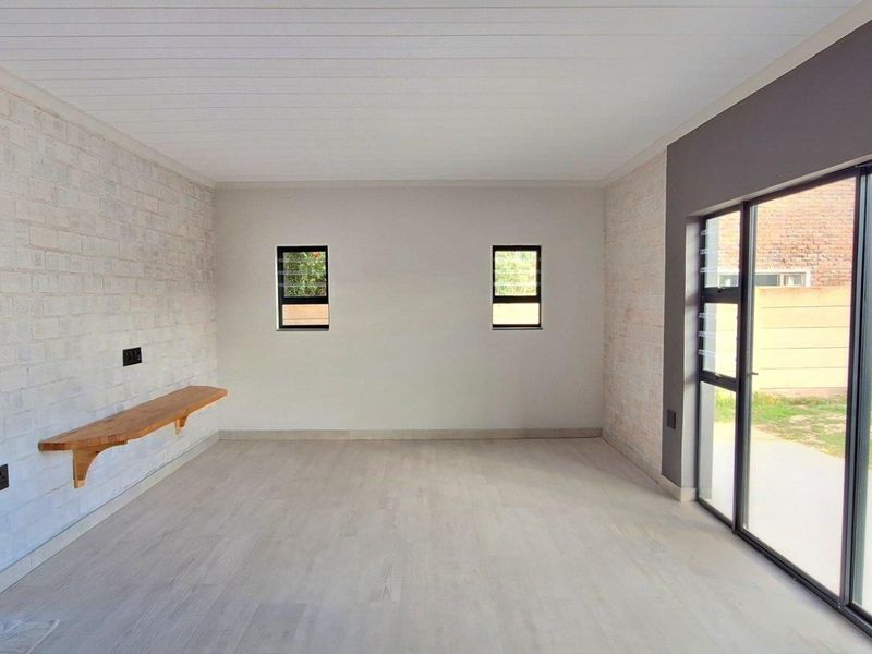 A bright, empty living room featuring exposed brick walls, light laminate flooring, and large sliding glass doors providing access to the garden.
