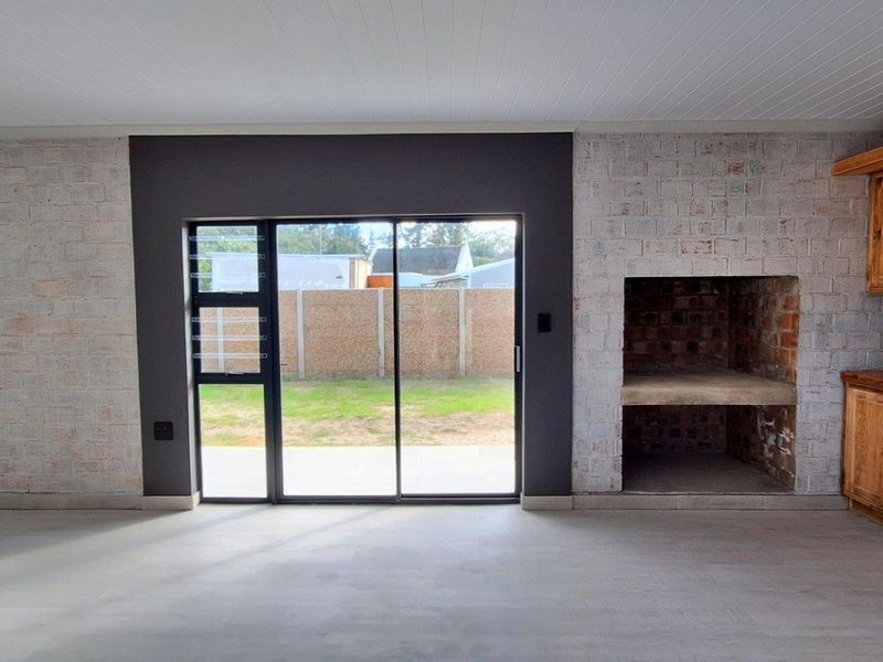 Spacious living area featuring a built-in fireplace, exposed brick accents, custom wooden cabinetry, and large sliding doors leading to the garden.