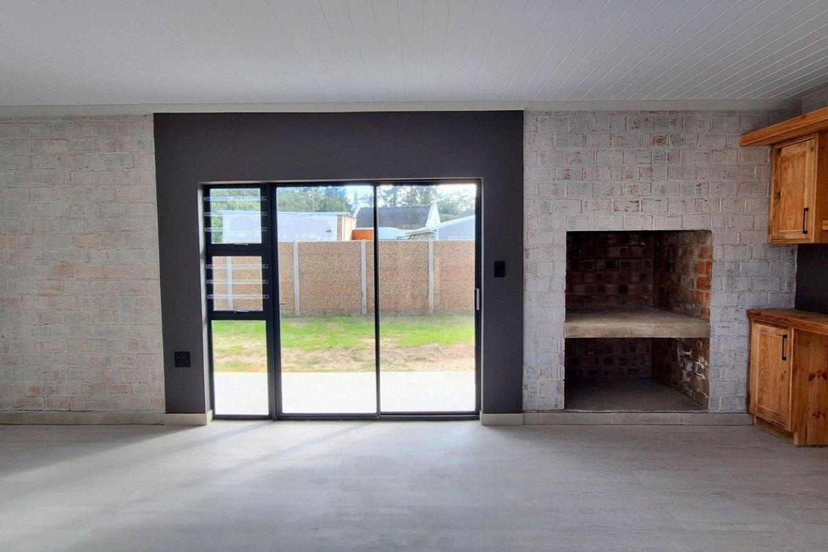 Spacious living area featuring a built-in fireplace, exposed brick accents, custom wooden cabinetry, and large sliding doors leading to the garden.