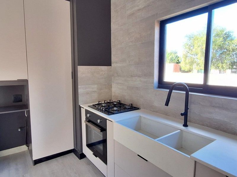 Modern kitchen featuring built-in oven, gas hob, double basin sink with matte black tap, and contemporary stone-look wall tiling.