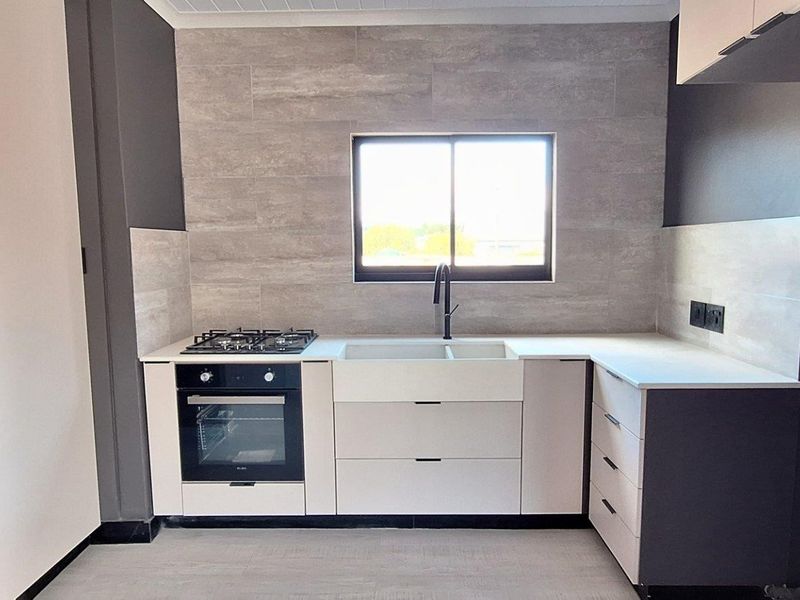 A modern, newly renovated kitchen featuring sleek cabinetry, stone countertops, a gas hob, built-in oven, and a stylish tiled backsplash.