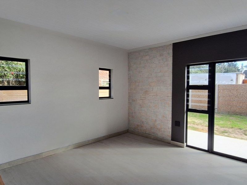 A bright, empty living area featuring modern tiled floors, an exposed brick accent wall, and large sliding doors leading to the garden.