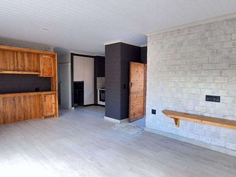 Spacious open-plan living area featuring a rustic exposed brick wall, built-in wooden cabinetry, and modern laminate flooring throughout.