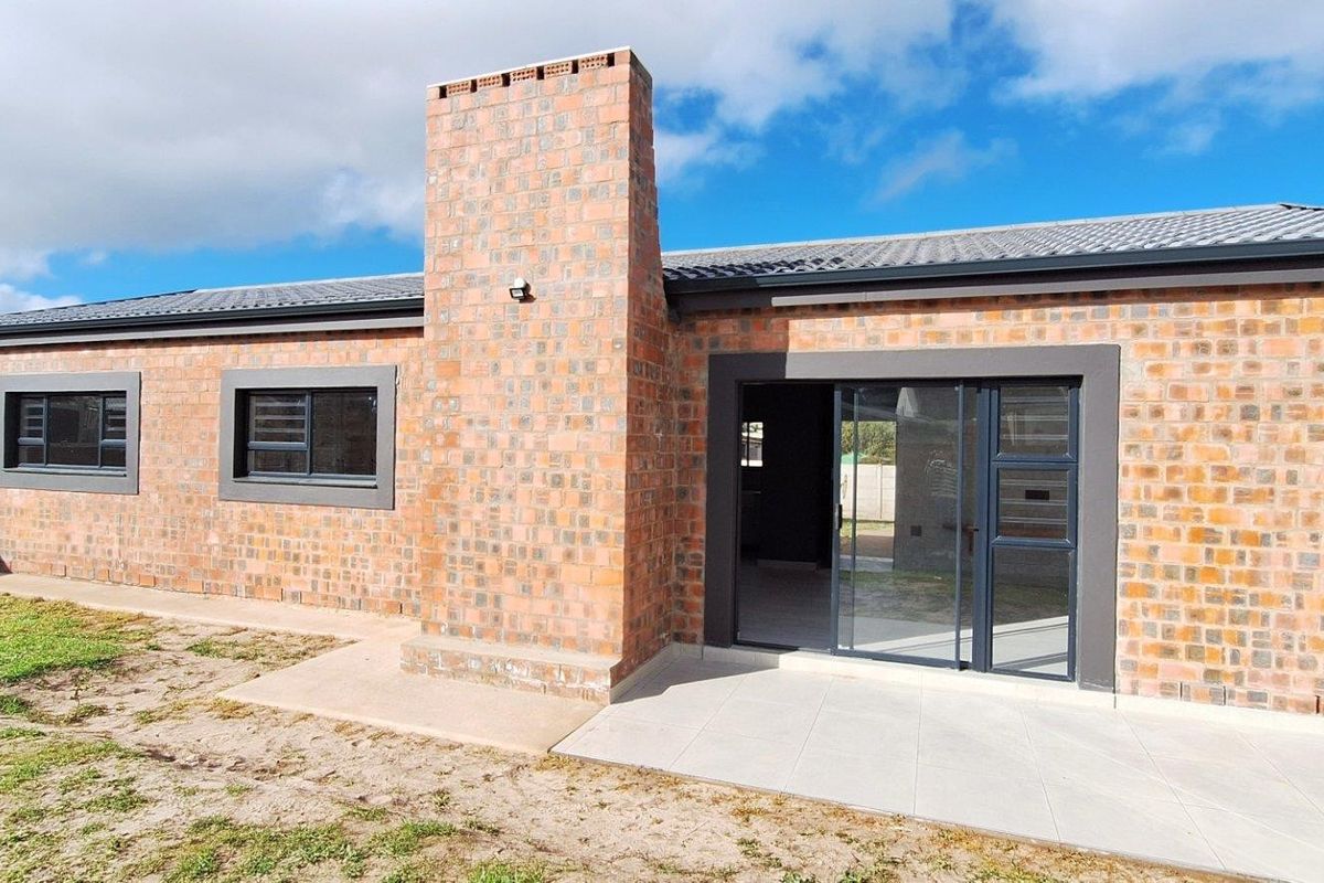 Rear view of a modern face-brick house featuring a tiled patio, sliding glass doors, and a prominent brick chimney stack.