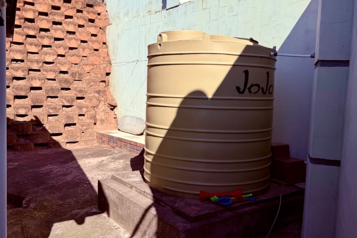 Rear exterior area featuring a large water storage tank on a concrete plinth, enclosed by a boundary wall and retaining structure.