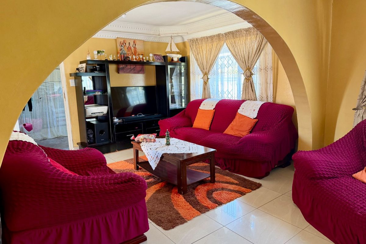 A living room featuring a prominent arched entryway, tiled flooring, and decorative ceiling cornicing, providing a traditional layout with ample natural light.