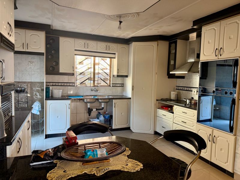 A functional kitchen featuring built-in cabinetry, a double basin sink, integrated oven, extractor fan, and tiled finishes throughout.