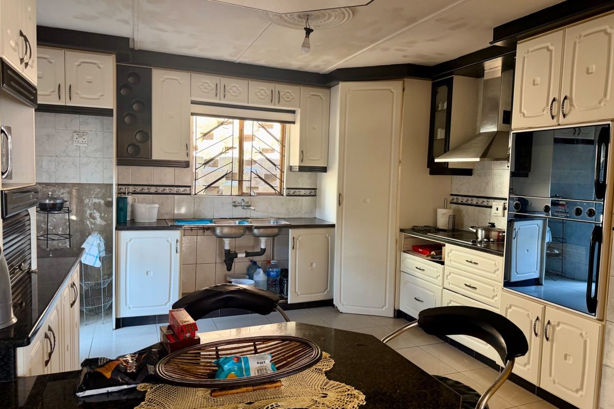 A functional kitchen featuring built-in cabinetry, a double basin sink, integrated oven, extractor fan, and tiled finishes throughout.