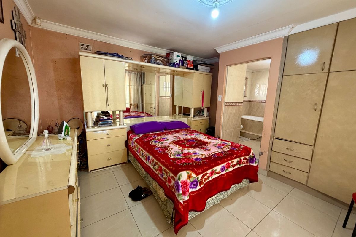 A bedroom featuring built-in cupboards, tiled flooring, and an en-suite bathroom. The room requires cosmetic updates to the wall finishes.