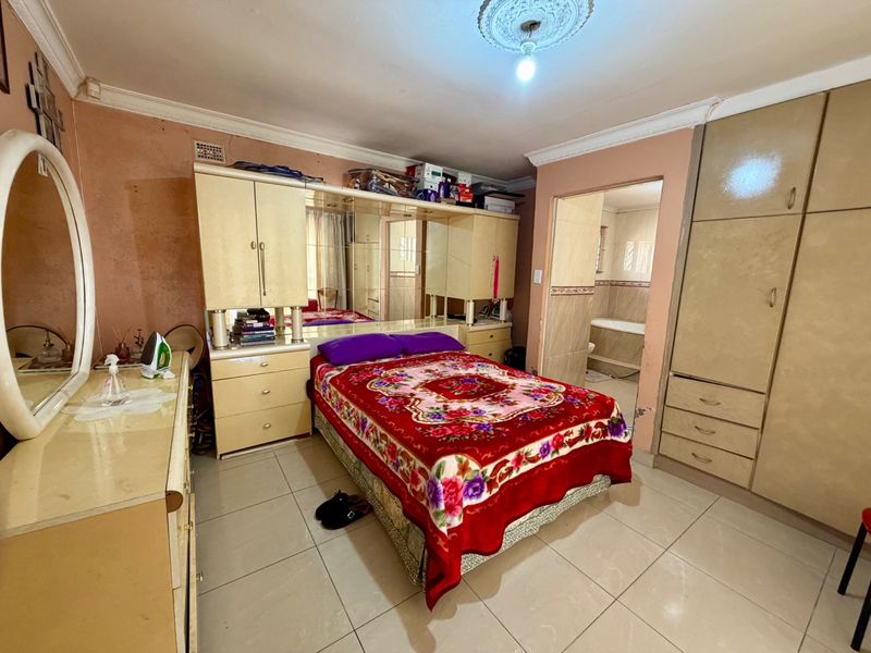 A bedroom featuring built-in cupboards, tiled flooring, and an en-suite bathroom. The room requires cosmetic updates to the wall finishes.