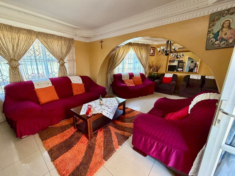 A spacious living room featuring decorative ceiling cornices, tiled flooring, and a distinctive arched wall opening connecting to an adjacent seating area.