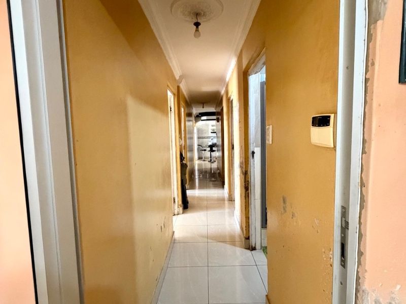 A long interior hallway featuring tiled flooring and a ceiling rose, currently showing significant wear to the wall finishes.