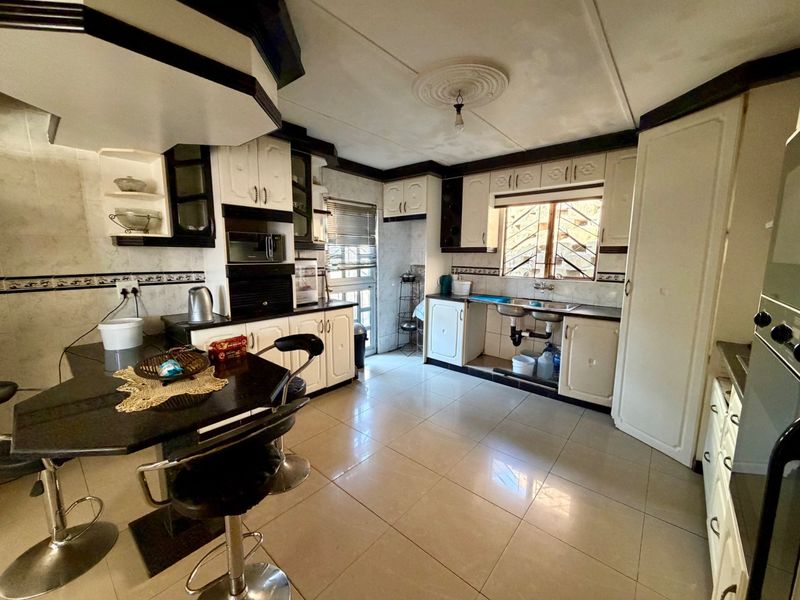 A dated kitchen featuring tiled flooring, built-in cabinetry, a breakfast bar, and a double basin sink with exposed plumbing.