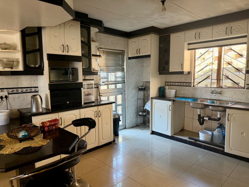 A dated kitchen featuring two-tone cabinetry, tiled flooring, and a double basin sink. The space requires minor repairs to cabinetry and plumbing.
