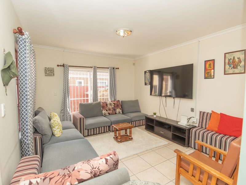 A functional living room featuring tiled flooring, a sliding door with security bars, and neutral wall finishes.